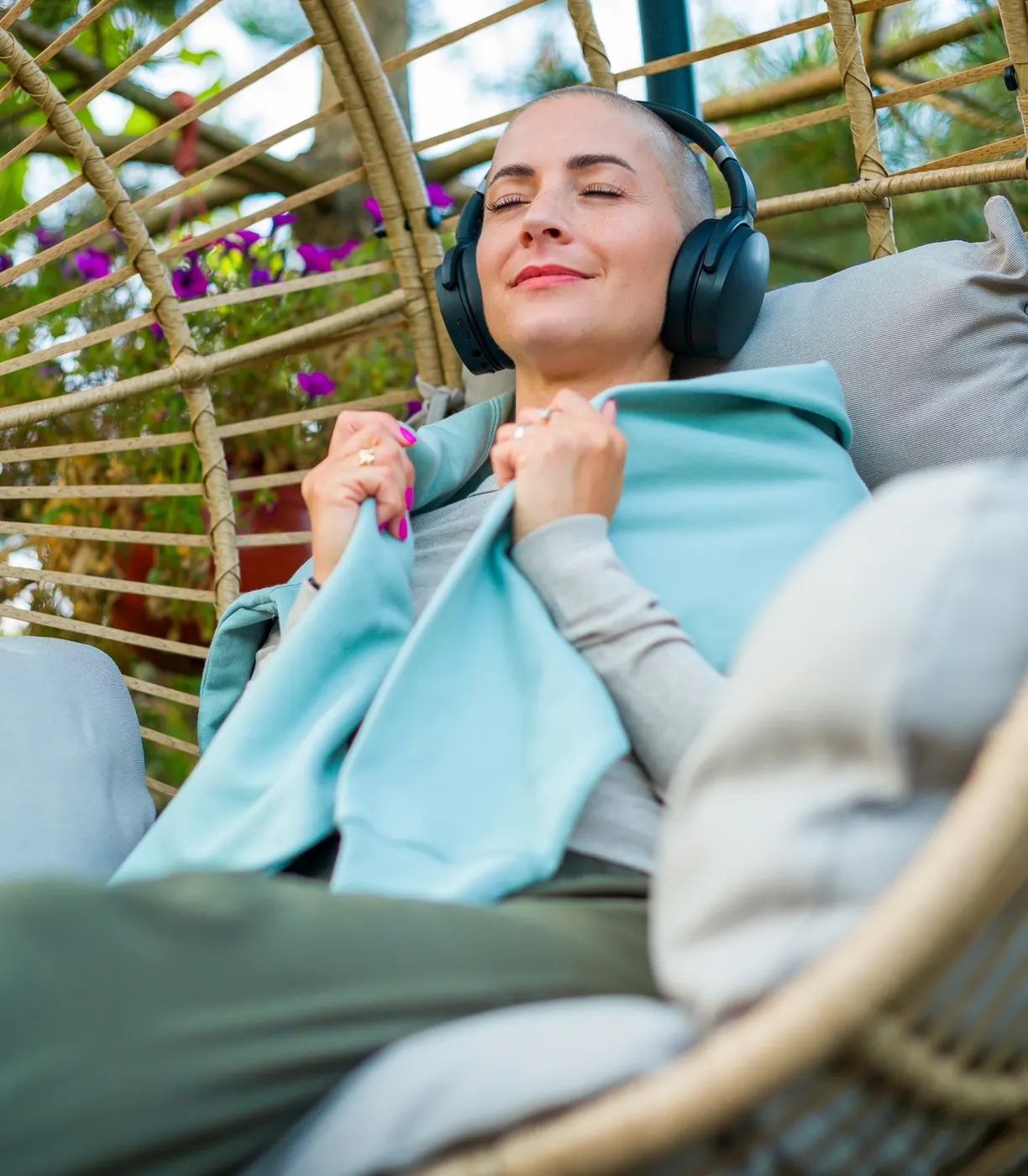 A woman rests calmly outdoors with her eyes closed and headphones on, a moment of steadiness after treatment.