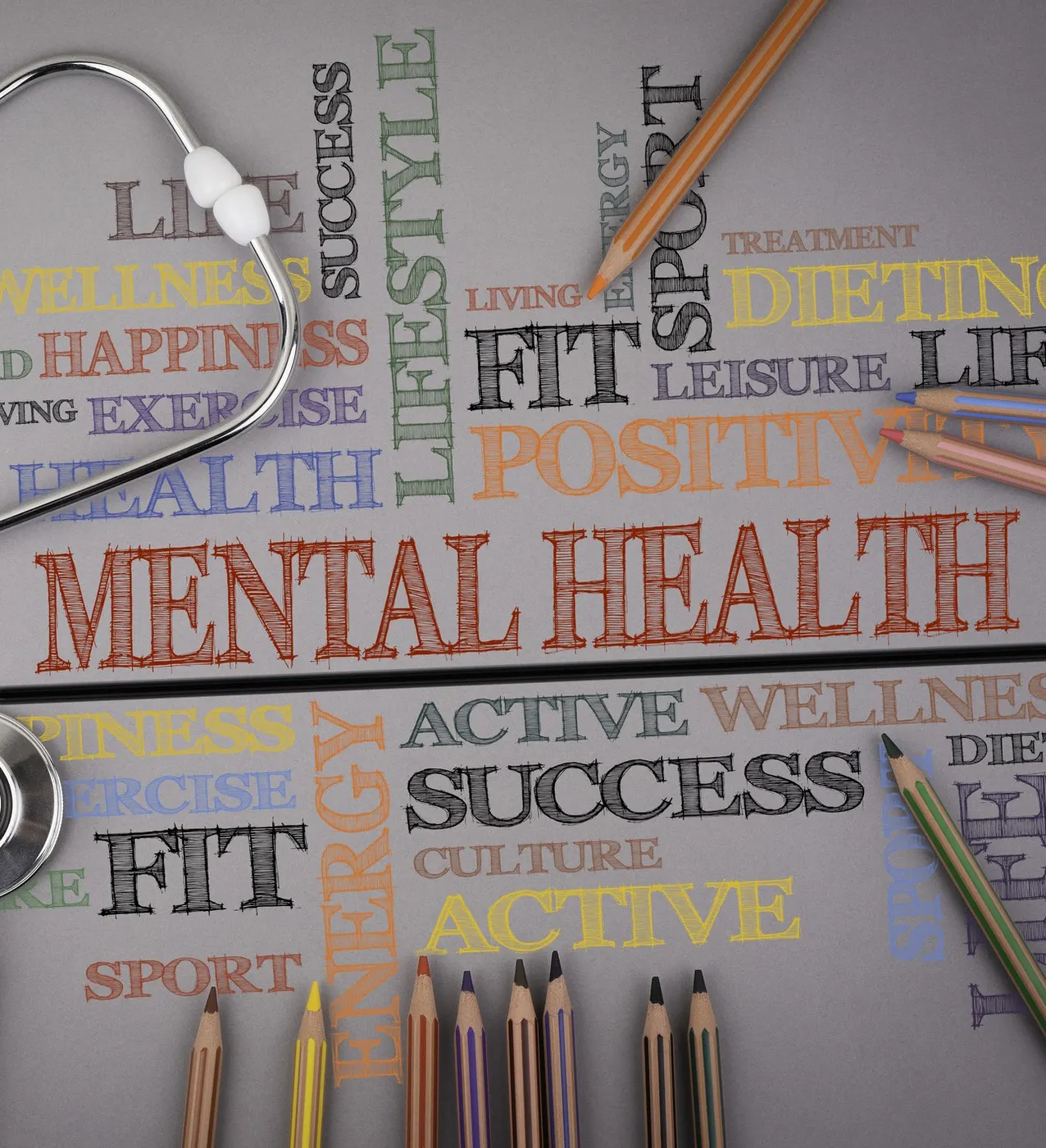 A desk flat lay of coloured pencils and a stethoscope over a word cloud with the words mental health, wellness and positive.